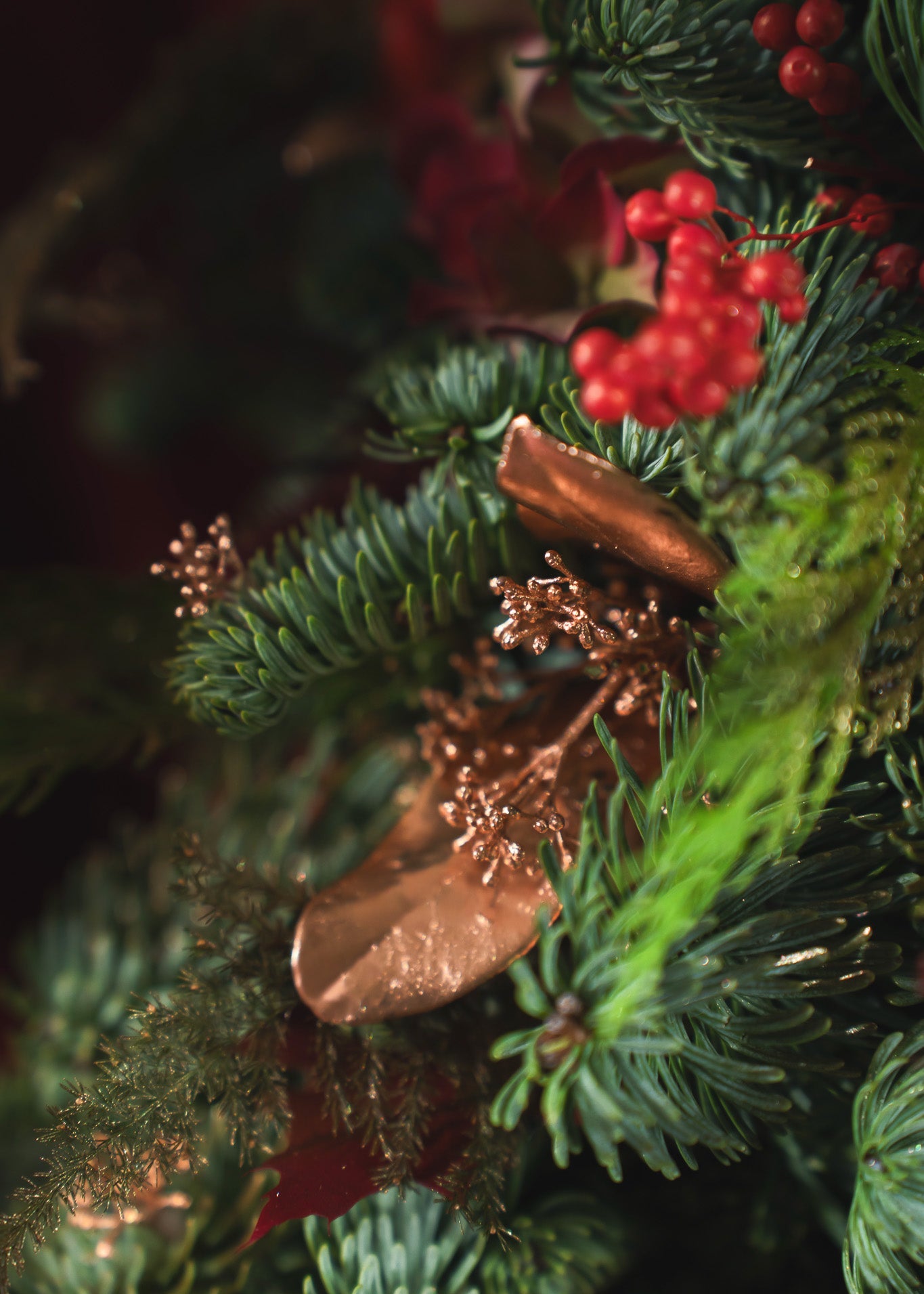 Close-up of a Christmas wreath with greenery, red berries, and copper leaves.