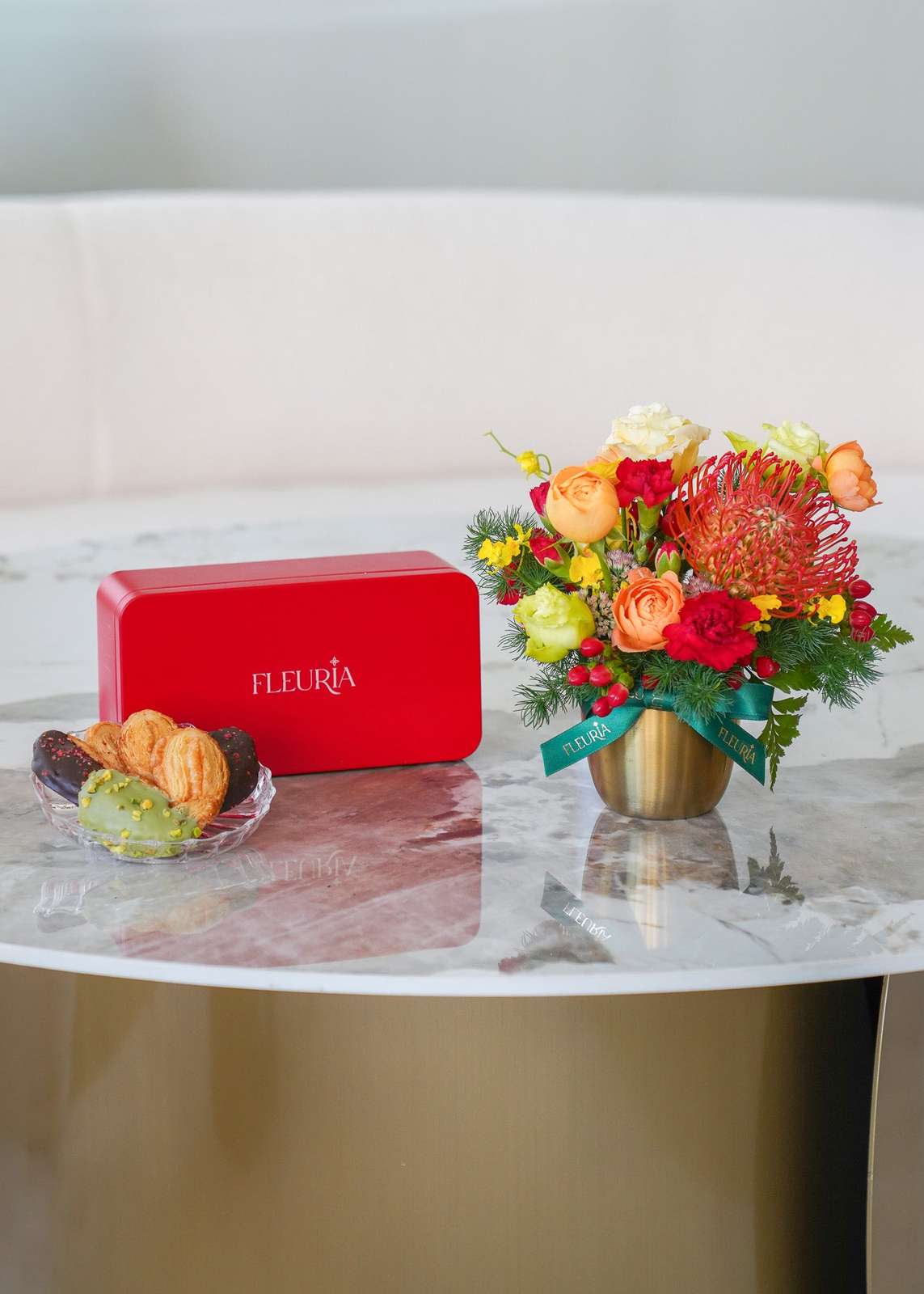 A red rectangular box with the brand name 'FLEURIA' on the front sits on a marble-topped table beside a small glass dish of p